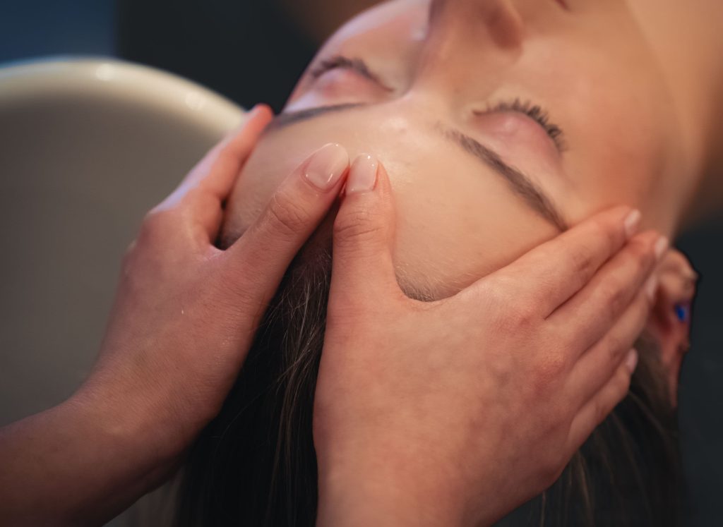 Therapist massaging a client's temples and hairline with both hands while the client rests with eyes closed.